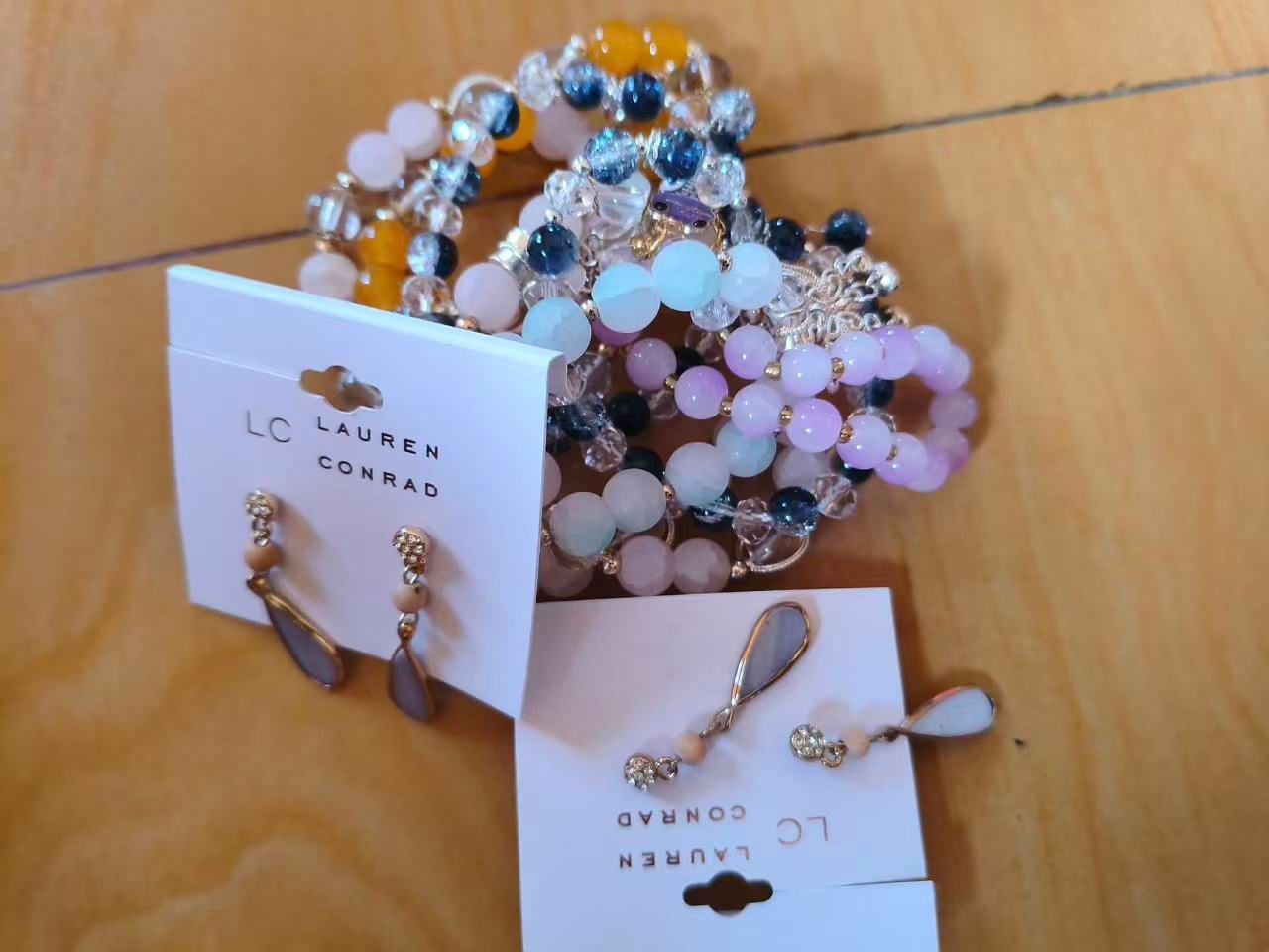 Beaded stretch bracelets and carded drop earrings arranged on a wooden floor.